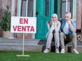 Fotografía de una pareja sentada a la puerta de su casa, con gesto de desánimo al no conseguir venderla.